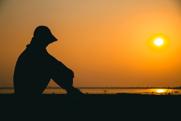 Silhouette of a young woman standing sadly looking at the sky at sunset