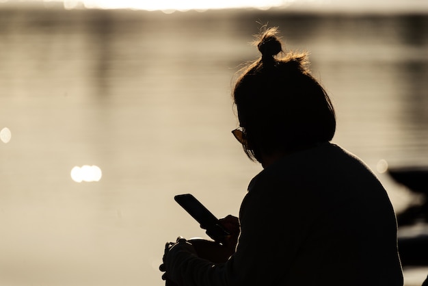 日没時にスマートフォンを使用して若い女性のシルエット