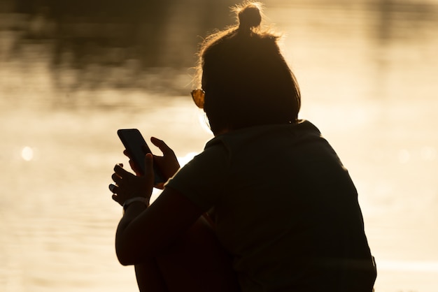 Силуэт молодой женщины с помощью смартфона во время заката
