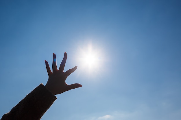 Silhouetted a female hand against a blue sky and bright sun