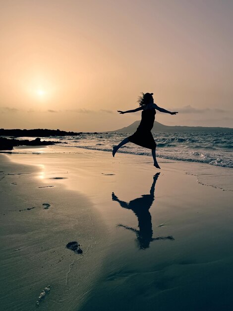 Photo silhouetted girl dancing at sunset on sandy beach playa del risco lanzerote canary islands