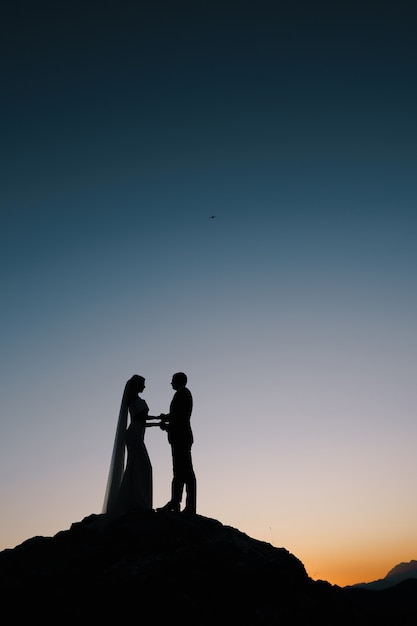 Silhouetten van de bruid en bruidegom staan op de berg aan de avondrood