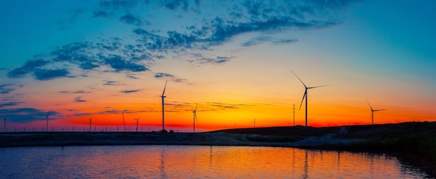 Silhouetten van de elektriciteitscentrale van windgeneratoren op het meer bij zonsopgang