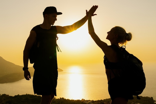 Silhouetten van een man en een vrouw die elkaar een high five geven en zich verheugen in het beklimmen van de bergen Zonsondergang in de bergen