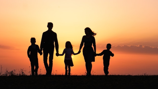 Foto silhouetten van gelukkige familie die de handen vasthoudt in de weide tijdens zonsondergang