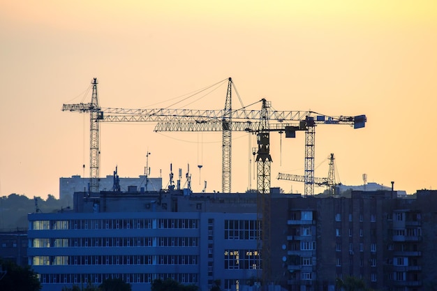 Silhouetten van het bouwen van kranen in de avondlucht tegen de achtergrond van de stedelijke bouwindustrie bij zonsondergang