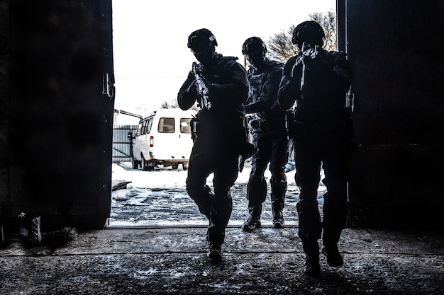 Foto silhouetten van het tactische team van speciale politie-operaties, swat-jagers die aanvalsgeweren richten terwijl ze schouder aan schouder in een helderwitte deuropening staan. bestormingsruimte voor militaire tactische groepen