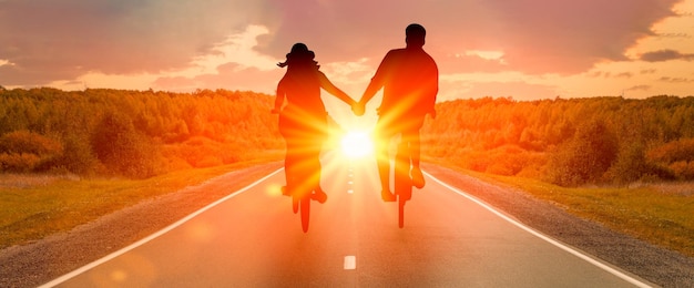 Silhouetten van man en vrouw hand in hand fietsen bij zonsondergang paar hand in hand en fietsen samen Romance love concept banner