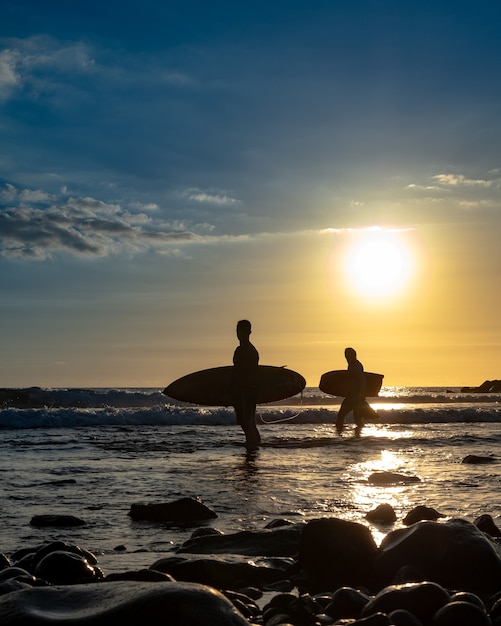 Silhouetten van surfers bij zonsondergang