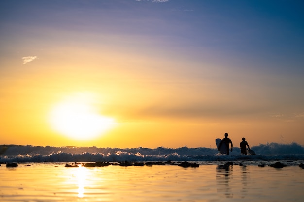 Silhouetten van twee mannen die bij zonsondergang surfen