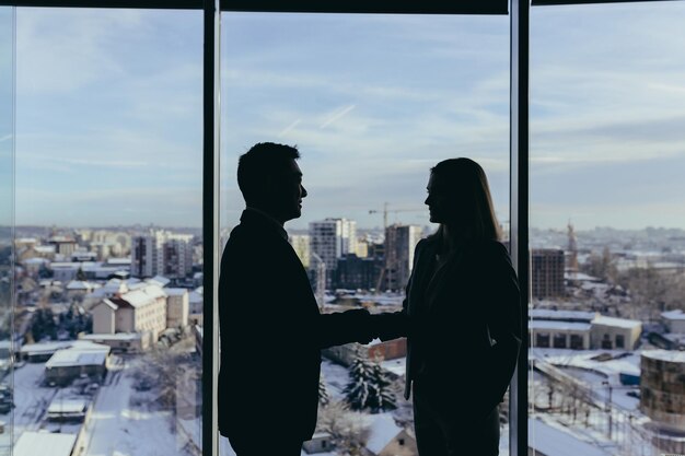 Silhouetten van twee medewerkers team van zakenlieden Aziatische man en vrouw overleggen en communiceren in een modern kantoor bij het raam