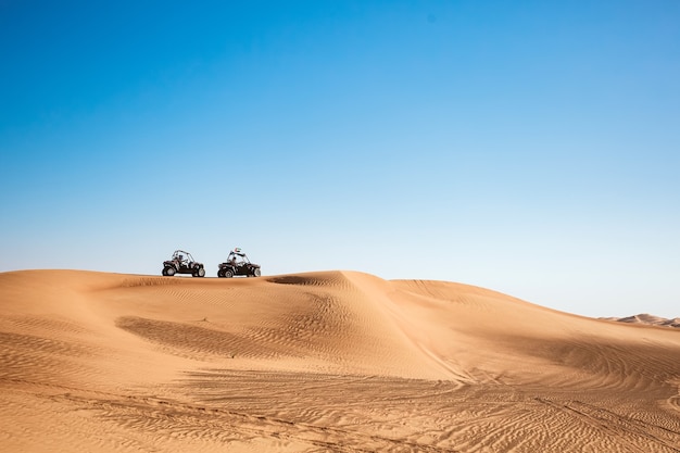 Silhouetten van twee quads met buggy's op een zandheuvel met lucht in de woestijn van Dubai