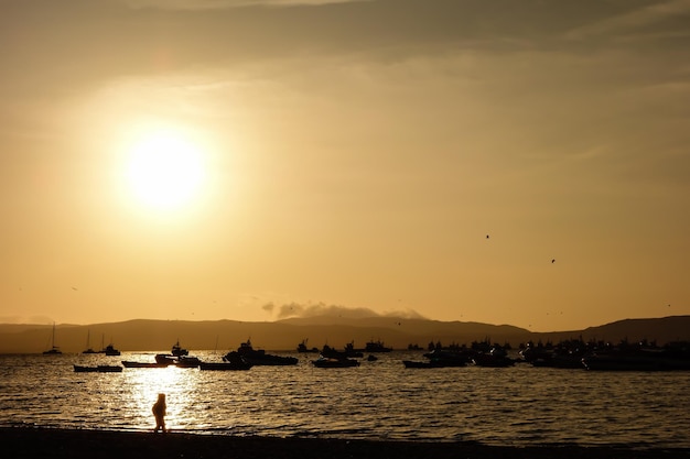 Paracas 해변의 만에서 소년과 보트의 실루엣 바다에 반사되는 일몰