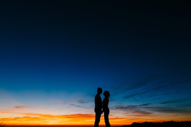 Silhouettes of a couple against the sunset in the mountains