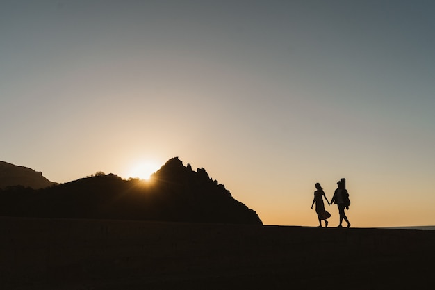 Silhouettes of a couple in love. Romantic photography near the mountains. A young couple is walking by the sea.