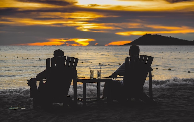 Silhouettes of couple relaxing on chairs on the beach