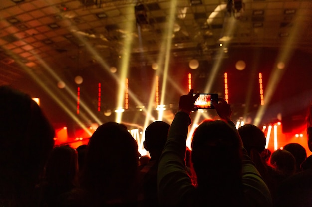 Sagome di folle di spettatori a un concerto con gli smartphone in mano. la scena è splendidamente illuminata da faretti.