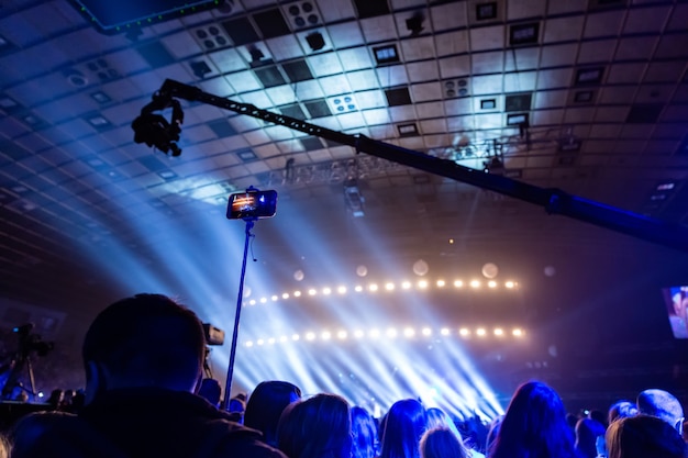 Silhouettes of crowds of spectators at a concert with smartphones in their hands. The scene is beautifully illuminated by spotlights.