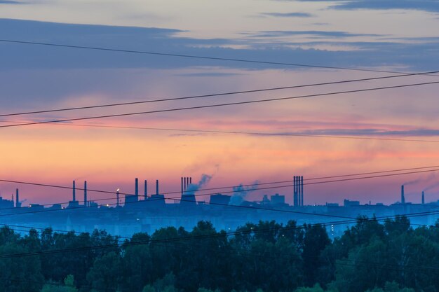 Silhouettes of factories and smoking chimneys at sunrise border
of forest and civilization