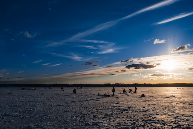 Siluette dei pescatori che pescano e viti del ghiaccio in inverno