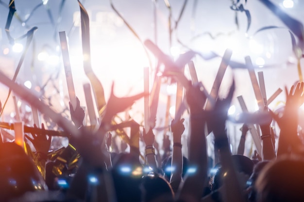 コンサートでの手のシルエット。ステージからの光。紙吹雪。手を上げた人々のシルエットの群衆。リボン