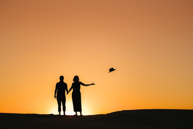 Sagome di una giovane coppia felice ragazzo e ragazza su uno sfondo di tramonto arancione nel deserto di sabbia