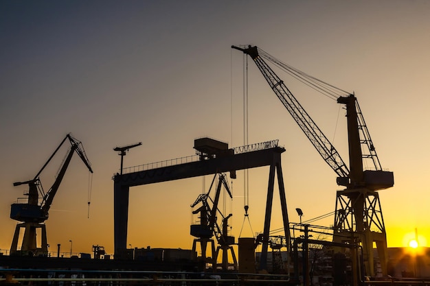 Silhouettes of harbor cranes at sunset Shipyard at sunset