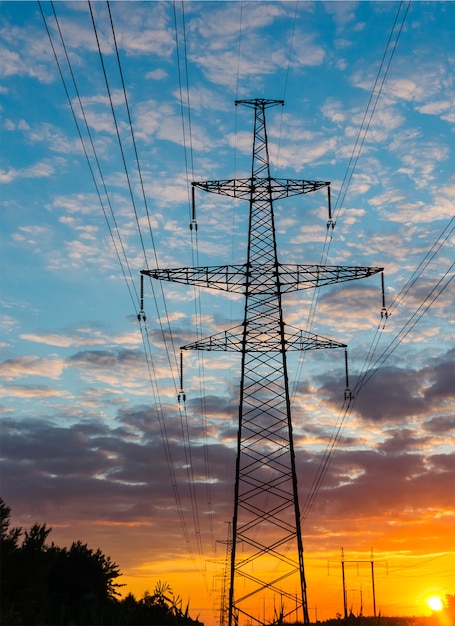 Silhouettes high voltage electric pylon in sunset background.