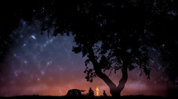 Silhouettes of a man with a dog by the fire against the background of the starry sky and the constellations of the universe