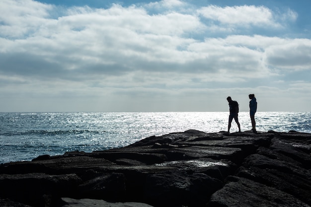 Силуэты мужчины и женщины на каменном пирсе против океана. Остров Лансароте, Испания.