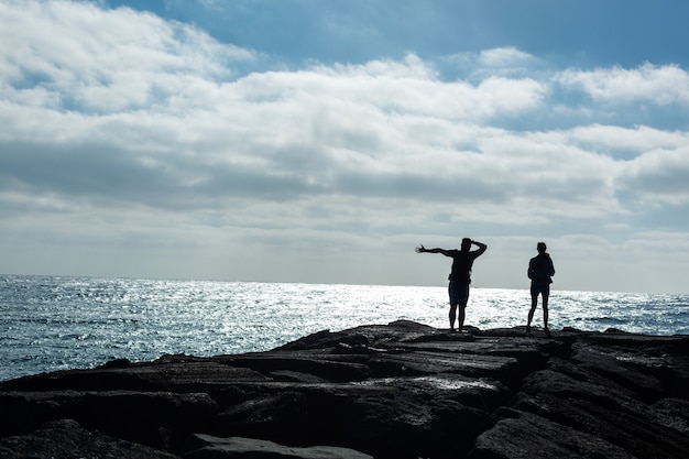 Silhouettes of a man and woman on a stone pier against the ocean. Island Lanzarote, Spain.