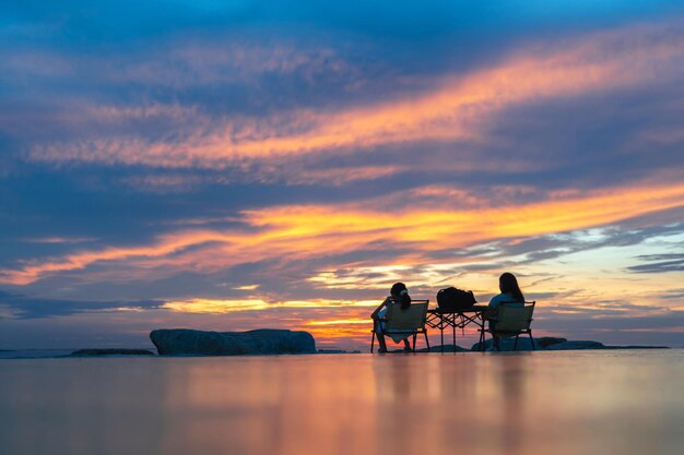 Фото Силуэты матери и дочери, сидящих на пляже на фоне заката вечернего неба