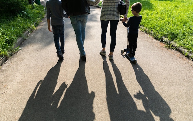 사진 백라이트에 젊은 사람들의 실루엣입니다. 젊은 가족 아빠, 엄마, 그리고 두 아이는 지는 햇살 아래 공원의 길을 따라 걷습니다.