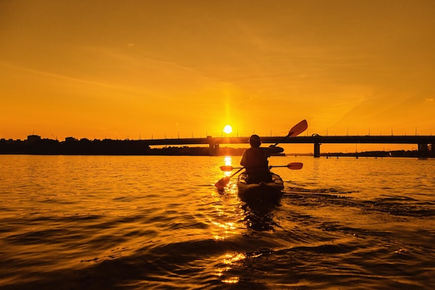 Photo silhouettes of people in kayak at sunset young married couple is boating on river