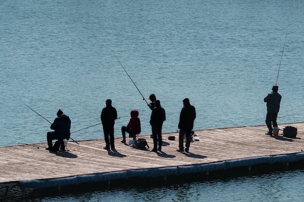 Silhouettes of people with fishing rods on the beach.