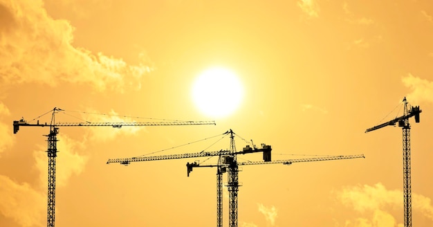 Silhouettes of tower construction cranes with yellow sky at\
morning time