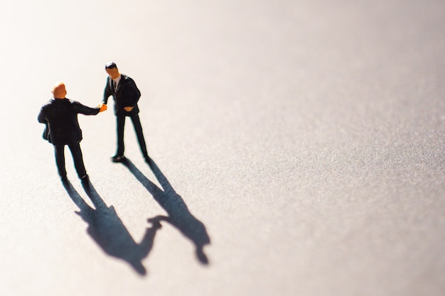 Silhouettes of two businessman, probably men, shaking their hands as a sign of an agreement or deal. The meeting takes place on floor  during the warn sunset.