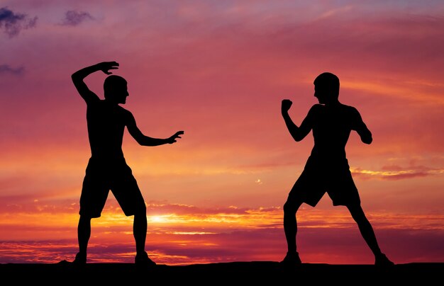 Silhouettes of two fighters on sunset fiery background