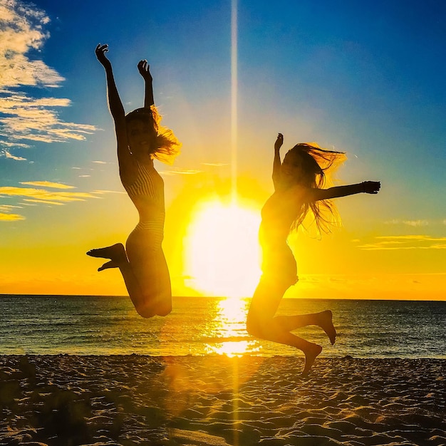 Silhouettes of two girls jumping infront of the sunrise on the beach