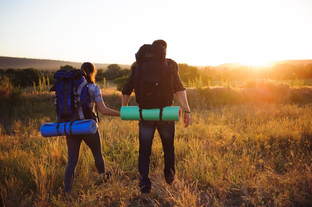 Silhouettes of two hikers with backpacks walking at sunset. Trekking and enjoying the sunset view