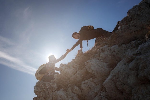 Silhouettes of two people climbing mountains and helping against the blue sky