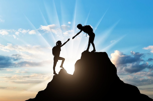 Silhouettes two women climber on top of the mountain. The concept of female mutual assistance