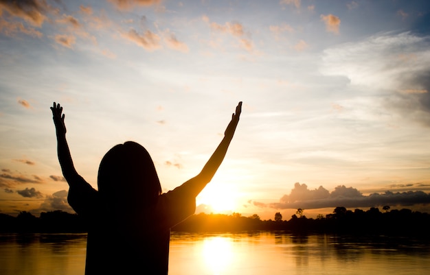 Silhouettes women praying hand over beautiful sun set background.
