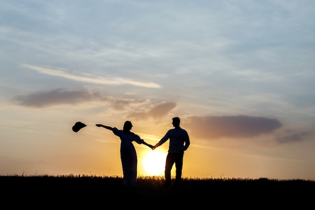 Photo silhouettes of a young couple on the horizon, in the background the sun is setting