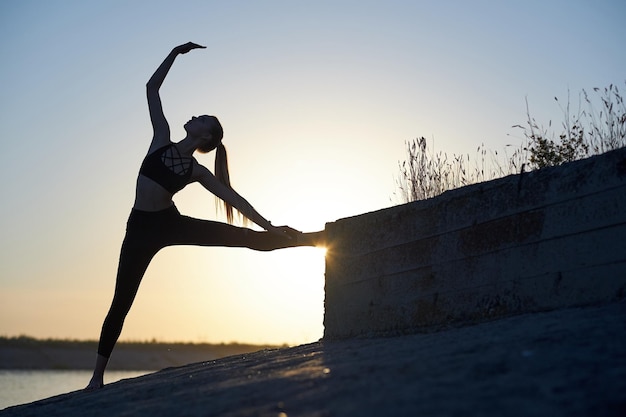 Silhouetvrouw het praktizeren yoga of het uitrekken zich op de strandpijler bij zonsondergang of zonsopgang