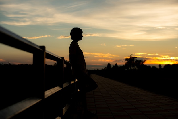 Silhouetvrouw met droefheid alleen bij zonsondergang.