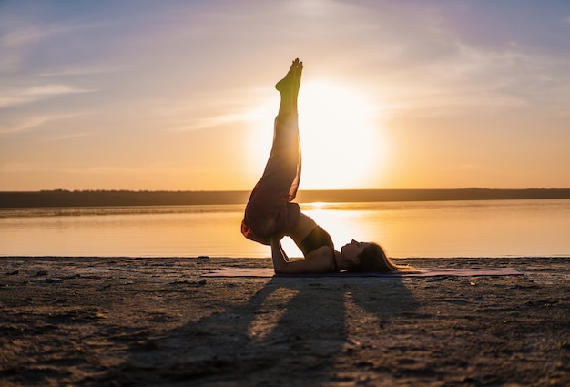 Foto silhouetvrouw op het strand bij zonsondergang die yogaasana doen. ochtend natuurlijke stretch warming-up training