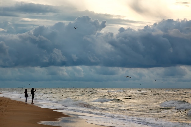 Silhuettes of two people makinf photo of dramatic sky on a morning seascape. 