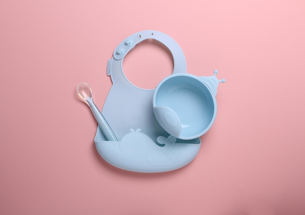 Silicone baby food accesory set on pink backgroundblue plate spoon and bib place for text copy space