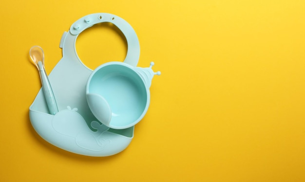 Foto accessorio per alimenti per bambini in silicone impostato su sfondo giallo blu cucchiaio e bavaglino per la copia del testo spa